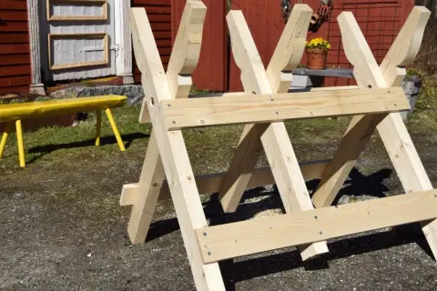 En nybyggd sågbock ritning i trä, redo för vedhuggning. En gul bänk syns i bakgrunden.
