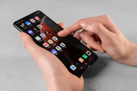 Dłoń dotyka ekranu smartfona z ikonami aplikacji. Dowiedz się, jak usunąć subskrypcję z telefonu, przeglądając ustawienia lub aplikacje.