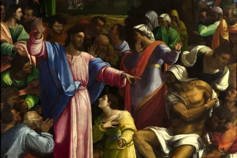 Jezus wskazuje na wskrzeszanego Łazarza. Tłum ludzi patrzy z podziwem i niedowierzaniem.
