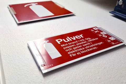 Röd skylt för pulverbrandsläckare, klassad brandklass A1. Informerar om att den släcker bränder i trä, tyg, papper, vätskor och gaser.