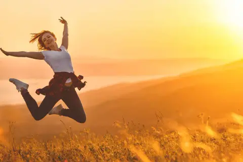 Eine Frau springt voller Freude in der goldenen Abendsonne. Sie ist voller Energie und genießt den Moment in der Natur.