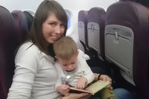 Mama z dzieckiem w samolocie Wizzair. Dziecko przegląda książeczkę, siedząc na kolanach mamy.