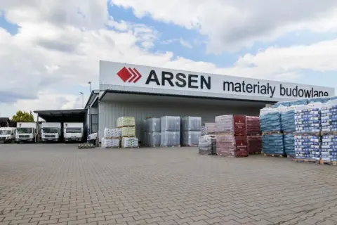 Budynek ARSEN materiały budowlane. Przed magazynem stoją ciężarówki i palety z materiałami. Sprawdź godziny otwarcia!
