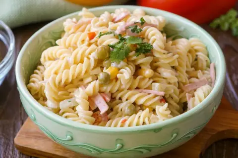 Ein cremiger Nudelsalat mit Erbsen, Mais und Schinkenwürfeln, der an einen herzhaften Fleischsalat erinnert. Garniert mit Petersilie.