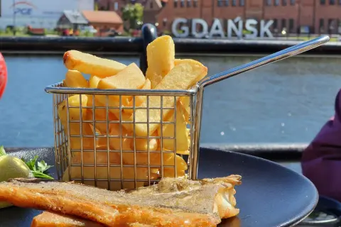 Ryba z frytkami na talerzu, w tle napis GDAŃSK. Idealne miejsce, gdzie zjeść w Gdańsku.