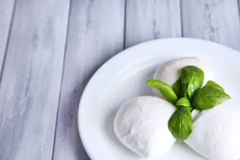 Trzy kulki mozzarelli z listkami bazylii na białym talerzu. Idealne do sałatki, a ich mozzarella kcal są niskie.