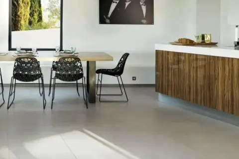 Un salon moderne avec une table en bois, des chaises noires design et un îlot de cuisine en bois. Le sol en carrelage clair complète l'ensemble.
