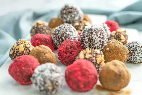 En hög med läckra dadelbollar recept, täckta med kokos, nötter och hallonpulver. Perfekta som energiboost!