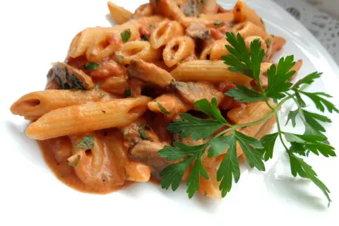 Penne z kremowym sosem pomidorowym i pieczarkami, udekorowane natką pietruszki. Pyszny makaron z pieczarkami.