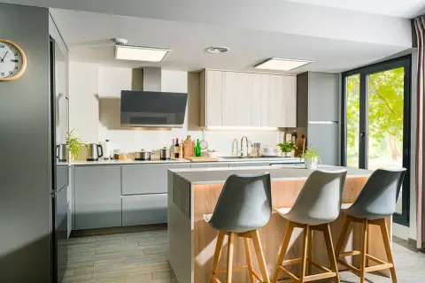 Moderna cocina con isla central, gabinetes grises y de madera, campana extractora negra y tres taburetes.