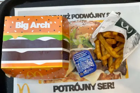 Duże frytki McDonald's w papierowym opakowaniu obok pudełka Big Arch i sosu.
