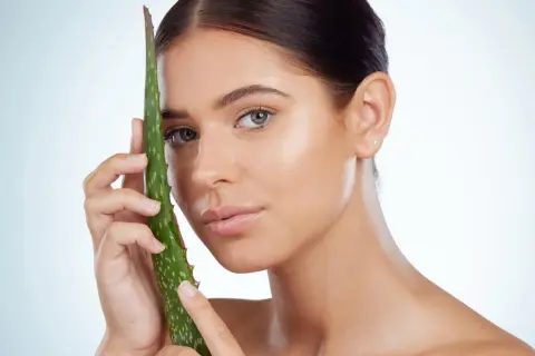 Mujer con piel radiante sosteniendo una hoja de aloe vera, ideal para el cuidado del aloe vera para la cara.