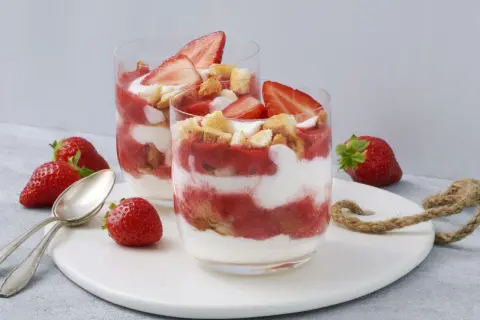 Zwei Gläser mit einem sommerlichen Dessert aus Erdbeeren und Sahne, garniert mit frischen Erdbeerscheiben und Keksstückchen. Ein schnell und einfach zubereitetes Genusserlebnis.