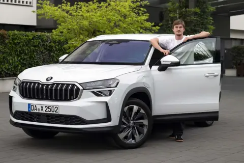 En ung man lutar sig mot en vit Skoda Kodiaq med öppen dörr. En spännande skoda kodiaq test.