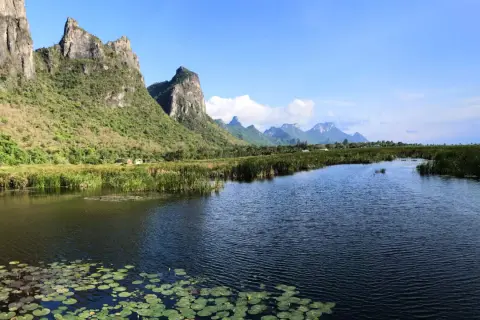 Khao Sam Roi Yot National Park: Majestätische Berge ragen über einen ruhigen Fluss mit Seerosen und Schilf auf.