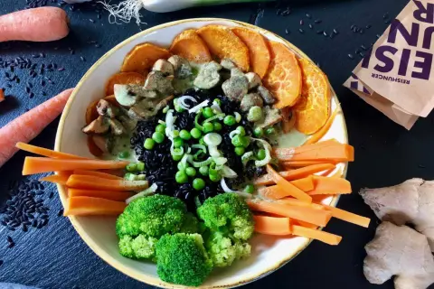 Bunter Reisschüssel mit schwarzem Reis, Süßkartoffeln, Brokkoli, Karotten, Erbsen und Pilzen in cremiger Sauce. Ein Gericht, das reich an Kohlenhydraten ist.