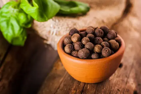 Garnek pełen aromatycznego ziela angielskiego na drewnianym blacie, obok zielone liście.