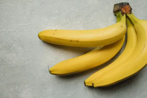 Trzy żółte banany leżą na szarym tle. Jeden banan kcal to zdrowa przekąska.