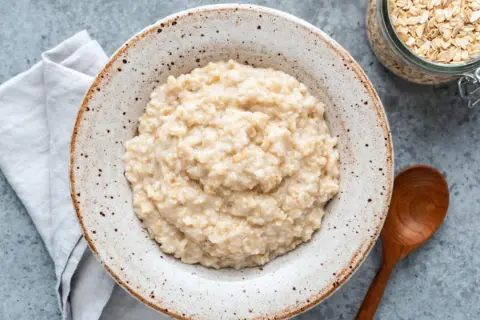Cremiger Porridge im rustikalen Teller, daneben Haferflocken im Glas. Ein einfaches Porridge Rezept für einen guten Start.