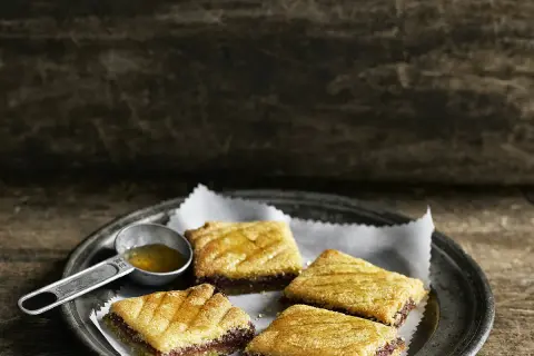 Quatre makrouts algériens sur une assiette, arrosés de miel. Une cuillère doseuse remplie de miel est à côté. Parfait pour une recette makrout algérien facile.