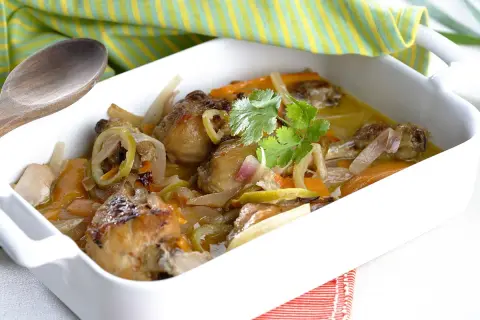 Muslitos de pollo guisados con verduras y limón, servidos en una cazuela blanca.