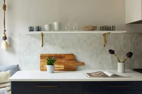 A kitchen backsplash features zellige tile, a Moroccan mosaic of hand-cut, glazed tiles. A wooden cutting board with a plant sits on the counter.