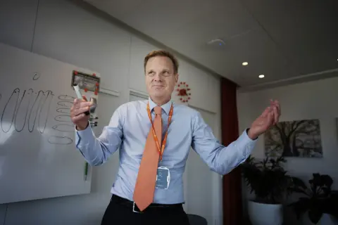 Swedbank vd med orange slips och namnskylt håller en penna vid en whiteboard.