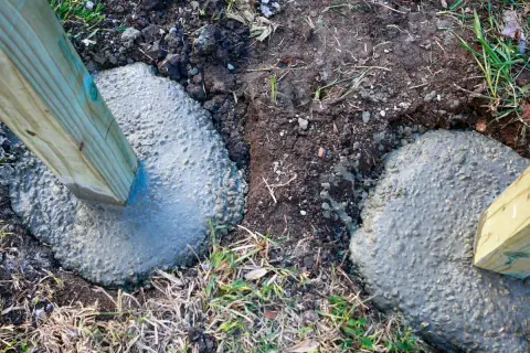 Holzpfosten werden in frischen Beton gesetzt. Die Tiefe, wie tief man einen Pfosten einbetonieren sollte, hängt von der Nutzung ab.