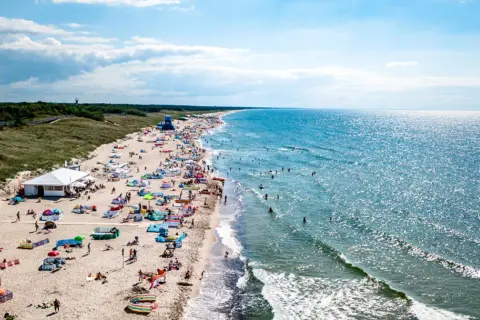 Tłum ludzi na plaży w Darłowie, gdzie można zwiedzić piękne wybrzeże i kąpać się w morzu.