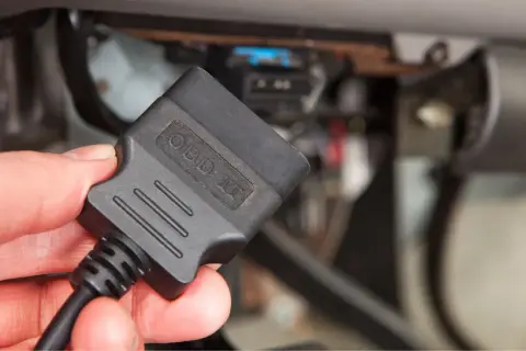 Dłoń trzyma czarny adapter OBD II, gotowy do podłączenia do złącza diagnostycznego pojazdu.