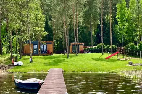 Idealne miejsce na wakacje w Polsce: drewniane domki, jezioro z łódką i plac zabaw dla dzieci.