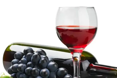 Czerwone wino w kieliszku, butelka i winogrona. Czy wiesz, że resweratrol co to jest, znajduje się w skórce winogron?