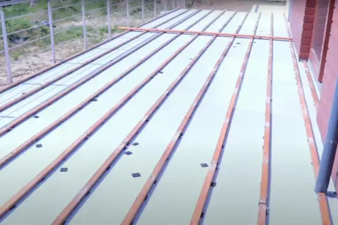 Drewniane legary ułożone na białej powierzchni, przygotowane do mocowania do betonu. Widać elementy mocujące.