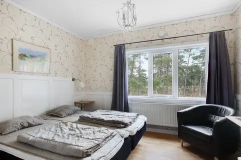 Mysigt rum på vandrarhem Gotland med två sängar, fåtölj och fönster med utsikt över skog.