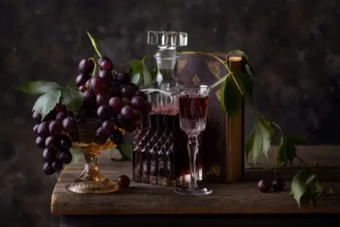 Kieliszek wina merlot veneto obok karafki i kiści winogron na drewnianym stole.
