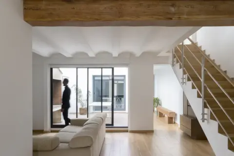 Interior moderno con vigas de madera, escaleras y un hombre mirando al patio. Estimación del precio construir casa 30 m2.