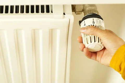 Mano che regola la manopola del termosifone, impostando la temperatura. Un gesto per svuotare termosifone e risparmiare energia.