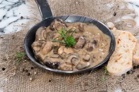Herzhafte Champignon Rahmsauce in einer Pfanne, garniert mit Rosmarin, serviert mit knusprigem Brot.