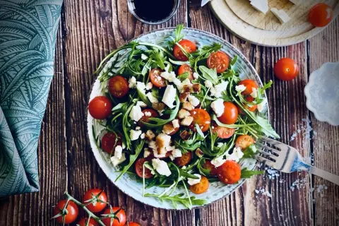 Frischer Rucola Salat mit Kirschtomaten, Feta und Croutons auf rustikalem Holztisch.
