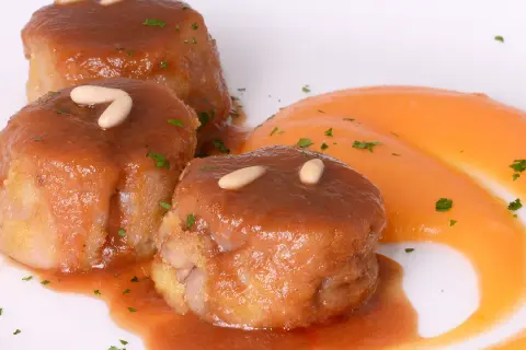 Deliciosas manitas de cerdo rellenas, bañadas en salsa y decoradas con piñones y perejil, acompañadas de puré de zanahoria.
