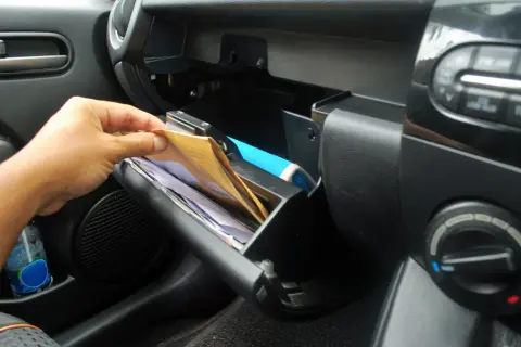 Ręka wyciąga dokumenty z schowka. Kierowca samochodu osobowego musi mieć przy sobie dowód rejestracyjny i polisę OC.