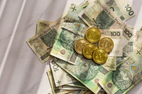 Złote monety Bitcoin leżą na stosie polskich banknotów 100 zł. Gdzie rozmienić pieniądze?