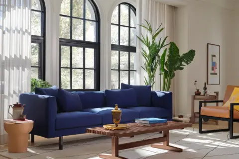 Granatowy salon inspiracje: nowoczesna sofa, drewniana ława, skórzany fotel i duże okna tworzą przytulną przestrzeń.