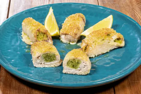 Involtini di pesce spada ripieni di erbe aromatiche, dorati e serviti su un piatto blu con spicchi di limone.