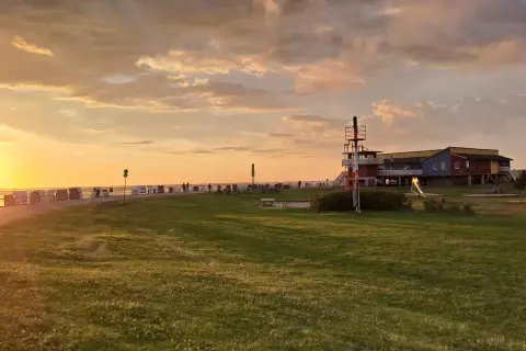 Sonnenuntergang am Husum Strand mit Strandkörben, einem Spielplatz und einem bunten Gebäude.