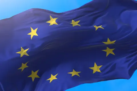 Flaga Unii Europejskiej falująca na wietrze na tle błękitnego nieba.