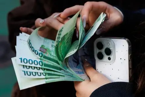 Dłonie liczą banknoty 10000 wonów, waluta Korei Południowej, obok białego etui na telefon.