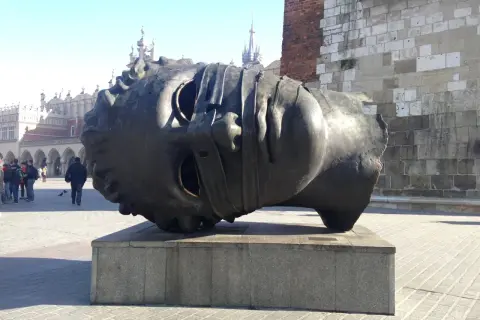 Gigantyczna, metalowa głowa leży na cokole. To intrygująca rzeźba, która przyciąga wzrok przechodniów na rynku.