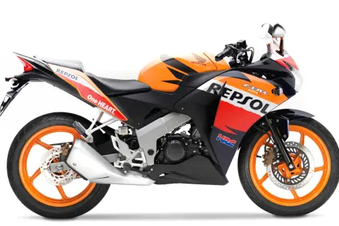 Pomarańczowo-czarny motocykl Honda CBR 125R w barwach Repsol, gotowy do jazdy z mocą V-max.