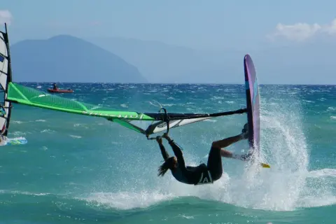 Windsurfer wykonuje akrobację na turkusowej wodzie, tworząc fontannę rozprysków.
